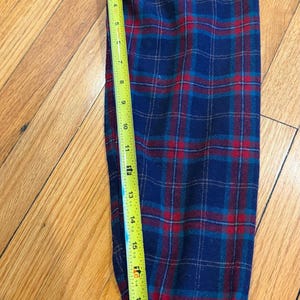 Puede incluir: Una manga de camisa de franela a cuadros azules, rojos y turquesas se mide con una cinta m&eacute;trica amarilla. La manga mide aproximadamente 51 cm de largo. El patr&oacute;n de cuadros es un dise&ntilde;o cl&aacute;sico.