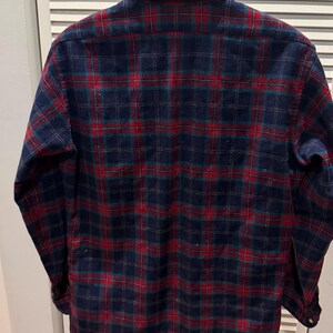 Puede incluir: Camisa de franela de manga larga con botones y un cl&aacute;sico estampado de cuadros. La camisa tiene una base azul marino con un dise&ntilde;o de cuadros rojos y verdes. La camisa se muestra en una percha blanca.