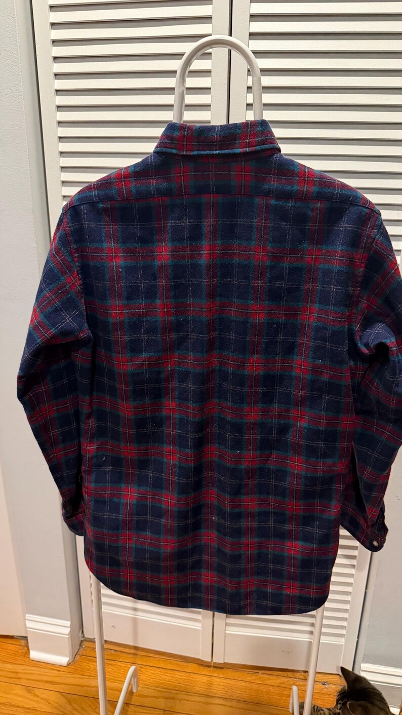 Puede incluir: Camisa de franela de manga larga con botones y un cl&aacute;sico estampado de cuadros. La camisa tiene una base azul marino con un dise&ntilde;o de cuadros rojos y verdes. La camisa se muestra en una percha blanca.