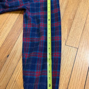 Puede incluir: Una camisa de franela a cuadros azul, rojo y turquesa con cuello abotonado y mangas largas. La longitud de la manga es de aproximadamente 71 cm.