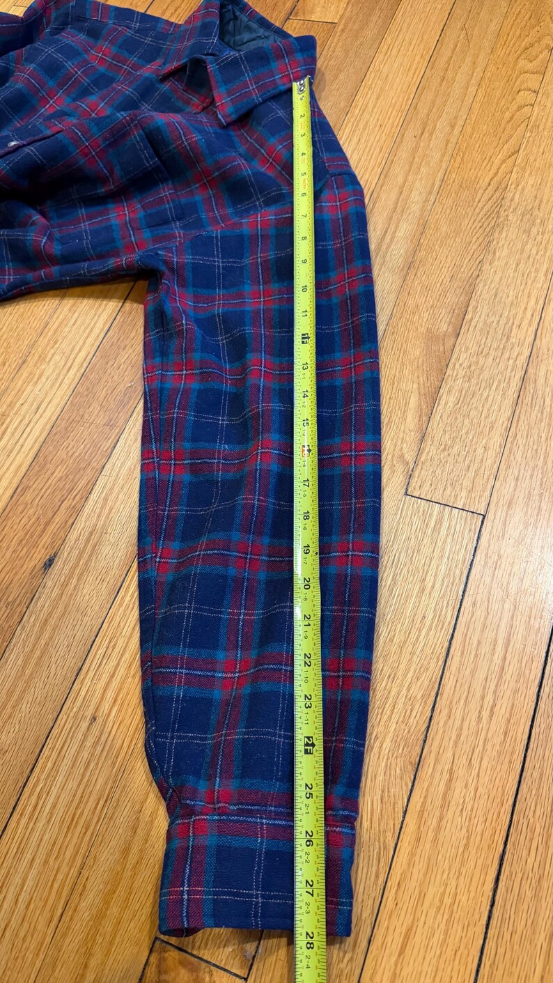 Puede incluir: Una camisa de franela a cuadros azul, rojo y turquesa con cuello abotonado y mangas largas. La longitud de la manga es de aproximadamente 71 cm.