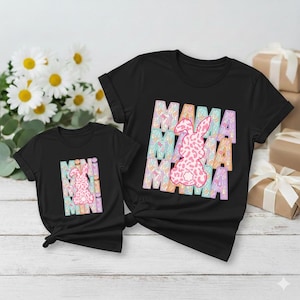May include: Two black t-shirts with the word "MAMA" in pastel colors and a pink bunny graphic. The shirts are short-sleeved and appear to be made of cotton. One shirt is larger than the other, suggesting a matching set for mother and child.