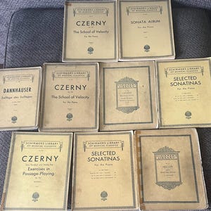May include: A collection of vintage piano music books from Schirmer's Library of Musical Classics. Titles include "Czerny: The School of Velocity," "Sonata Album," and "Selected Sonatinas." The books have aged, cream-colored covers with black text.