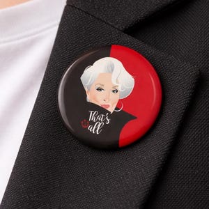 Pode incluir: Um botão redondo com um retrato de uma mulher com cabelo branco e o texto "That's all". O botão tem um esquema de cores preto e vermelho e está preso a um blazer preto.