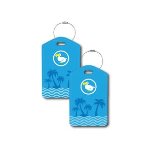 Puede incluir: Dos etiquetas de equipaje azules con un dodo blanco y palmeras sobre un fondo azul. Las etiquetas tienen un lazo plateado para sujetar al equipaje.