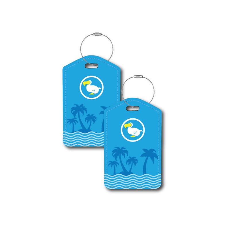 Puede incluir: Dos etiquetas de equipaje azules con un dodo blanco y palmeras sobre un fondo azul. Las etiquetas tienen un lazo plateado para sujetar al equipaje.