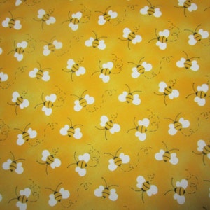 May include: A vibrant yellow fabric featuring a repeating pattern of small bees with black and yellow striped bodies and white wings. Each bee is depicted in a different orientation, accompanied by a small, dashed black line indicating flight paths.