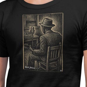 May include: Black t-shirt featuring a sepia-toned illustration of a musician playing a guitar in a recording studio. The image shows a man in a suit and hat seated on a chair, with a microphone and audio equipment visible. The artist's signature is at the bottom.