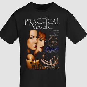 May include: A black short-sleeve t-shirt featuring a graphic print from the movie Practical Magic. The design includes portraits of two women, lit candles, a silhouette of figures with umbrellas, and the text: Practical Magic. For two sisters from a family of witches, falling in love is the trickiest spell of all.
