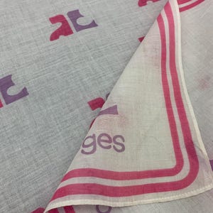 Peut inclure: Un foulard gris clair et blanc avec un motif r&eacute;p&eacute;t&eacute; de lettres stylis&eacute;es roses et violettes. Le bord du foulard a une bordure rose avec le mot "ges" imprim&eacute; en violet.