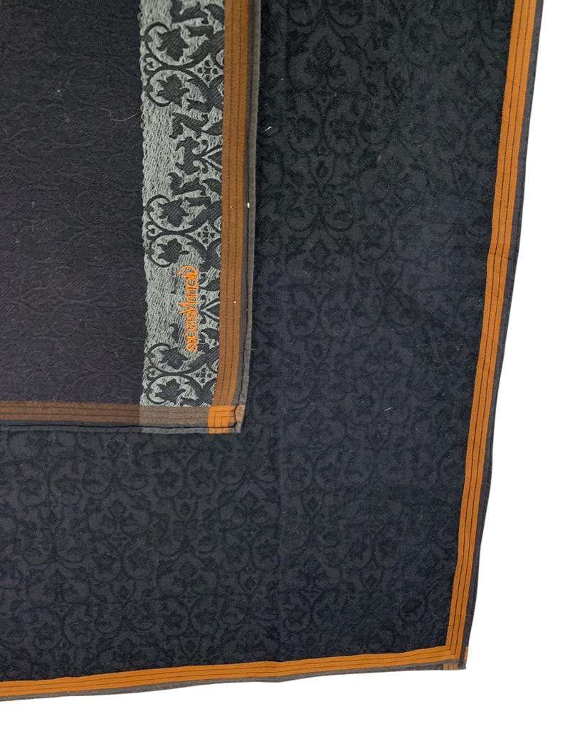 Puede incluir: Un pa&ntilde;uelo gris oscuro con un dise&ntilde;o floral. El pa&ntilde;uelo tiene un borde con una franja marr&oacute;n y naranja. La esquina del pa&ntilde;uelo tiene un dise&ntilde;o gris y negro con el texto "Skevi Vintige" en naranja.