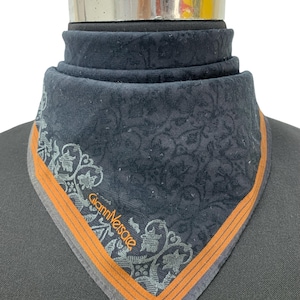 Könnte beinhalten: Ein dunkelmarinefarbenes Tuch mit einem verzierten floralen Muster und einem orangefarbenen Rand. Der Schal trägt den Text "Gianni Versace" in silberner Schrift. Das Tuch wird auf einer Schaufensterpuppe präsentiert.