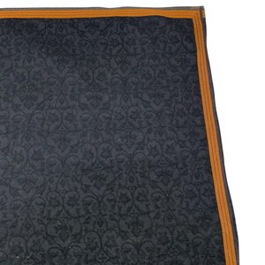 Puede incluir: Un textil gris oscuro con un patr&oacute;n floral repetido. El borde est&aacute; adornado con un fino borde naranja. La tela tiene un brillo sutil y el dise&ntilde;o es intrincado y detallado.