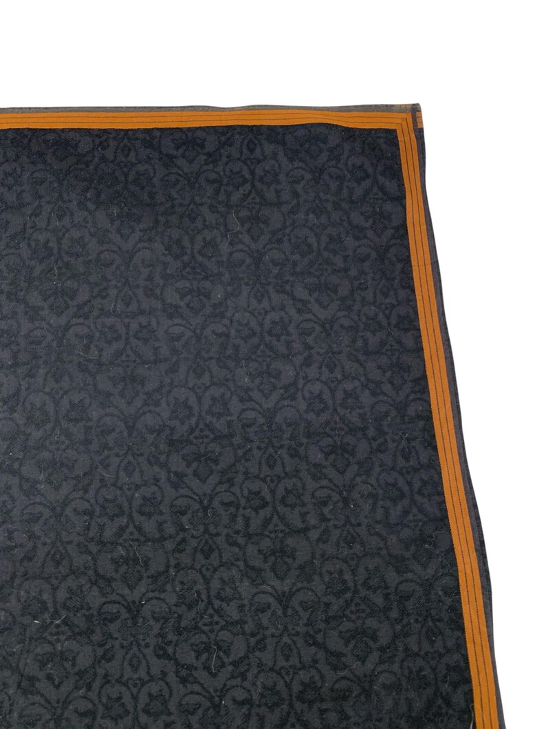 Puede incluir: Un textil gris oscuro con un patr&oacute;n floral repetido. El borde est&aacute; adornado con un fino borde naranja. La tela tiene un brillo sutil y el dise&ntilde;o es intrincado y detallado.