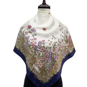 Könnte beinhalten: Quadratisches Seidentuch mit floralem Design in Rosa, Lila und Grün auf weißem Grund. Der Schal hat einen marineblauen Rand und den Text "BELLA ROSA".