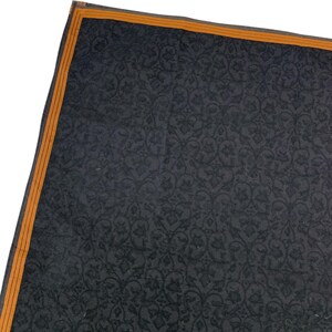Puede incluir: Una secci&oacute;n de un textil gris oscuro con un patr&oacute;n floral repetitivo. El borde est&aacute; bordeado con una fina franja naranja. El textil tiene un brillo sutil, lo que sugiere una tela lujosa.
