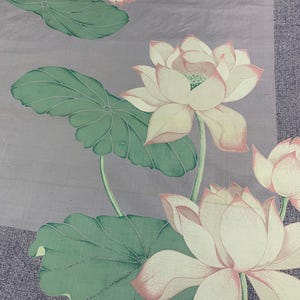 May include: A floral textile featuring a repeating pattern of lotus flowers and leaves. The flowers are white with pink edges, and the leaves are green. The background is a muted purple with a textured appearance, and a pink stripe runs along the bottom.