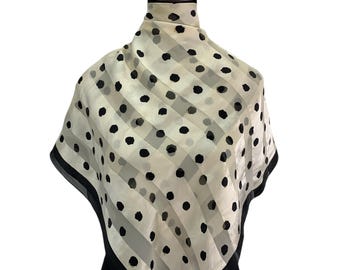 Puede incluir: Un pañuelo cuadrado color crema con lunares negros y rayas diagonales. El pañuelo tiene un borde negro y se muestra en un maniquí. El pañuelo está hecho de un material ligero.