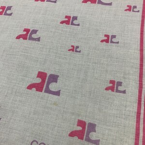 Peut inclure: Un mouchoir Courr&egrave;ges gris clair avec un motif r&eacute;p&eacute;t&eacute; de logos "AC" roses et violets. La bordure et le texte "courr&egrave;ges" sont roses. Le tissu a une texture subtile.