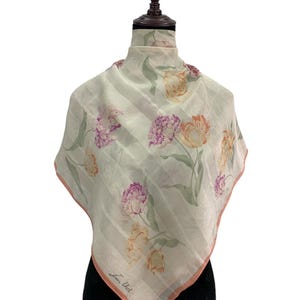 Peut inclure: Foulard carré à motifs floraux, avec un fond blanc et des rayures verticales. Le foulard présente des motifs de fleurs roses, violettes et jaunes. Il a une bordure rose clair. Le texte "Jean Urd" est visible dans le coin.