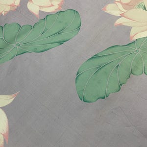 May include: A close-up of a fabric with a floral pattern. The design features large, light yellow lotus flowers with pink edges and green leaves on a gray background. The fabric has a subtle texture.