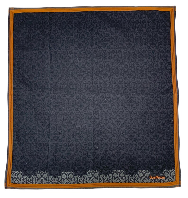Puede incluir: Un pa&ntilde;uelo cuadrado azul oscuro con un intrincado estampado floral. Tiene un borde naranja fino y un borde floral decorativo gris y blanco en la parte inferior. La marca "Gian Versace" est&aacute; impresa en naranja.