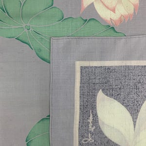 May include: A close-up of a gray textile with a floral design. The design features large green leaves and white lotus flowers with pink tips. A rectangular section with text is visible.