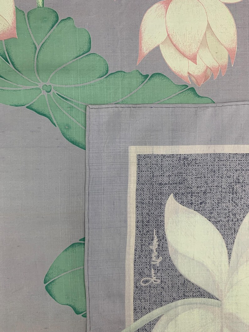 May include: A close-up of a gray textile with a floral design. The design features large green leaves and white lotus flowers with pink tips. A rectangular section with text is visible.