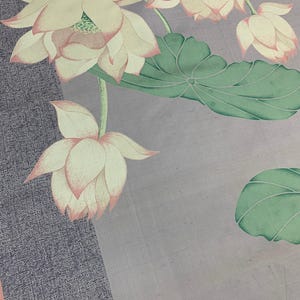 May include: A floral textile featuring a watercolor design of lotus flowers and leaves. The flowers are a soft cream color with pink edges, and the leaves are green. The background has a textured gray and light purple color scheme.