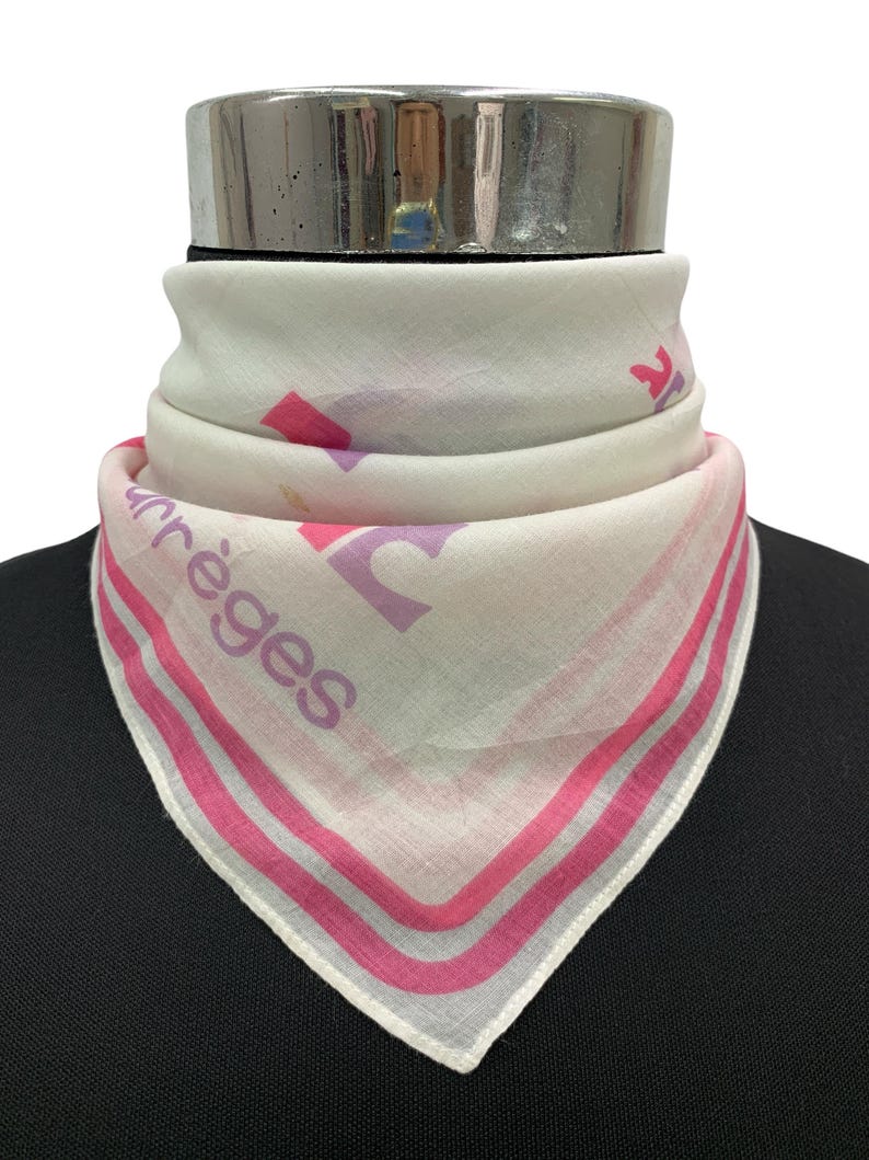 Peut inclure: Foulard blanc avec un motif rose et le mot "arr&egrave;ges" imprim&eacute;. Le foulard, de forme triangulaire, est pli&eacute; autour d'une forme noire. Il pr&eacute;sente des rayures roses sur les bords.