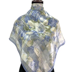 Puede incluir: Un pañuelo cuadrado con un estampado floral de rosas azules y blancas y hojas verdes. El pañuelo tiene un diseño a rayas azul claro y blanco y un borde azul claro. El pañuelo se exhibe en un maniquí.