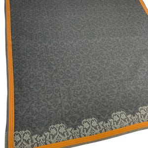 Puede incluir: Un textil cuadrado gris oscuro con un estampado floral en toda la superficie. El borde es de color naranja brillante con una fina raya gris. Un dise&ntilde;o floral decorativo recorre un borde.