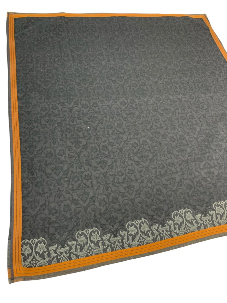 Puede incluir: Un textil cuadrado gris oscuro con un estampado floral en toda la superficie. El borde es de color naranja brillante con una fina raya gris. Un dise&ntilde;o floral decorativo recorre un borde.