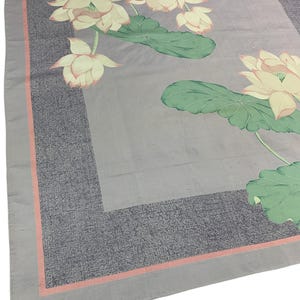 May include: A square, light gray scarf with a floral design. The scarf features a border of dark gray with a thin, salmon-colored stripe. The floral design includes lotus flowers in shades of cream and pink, with green leaves.
