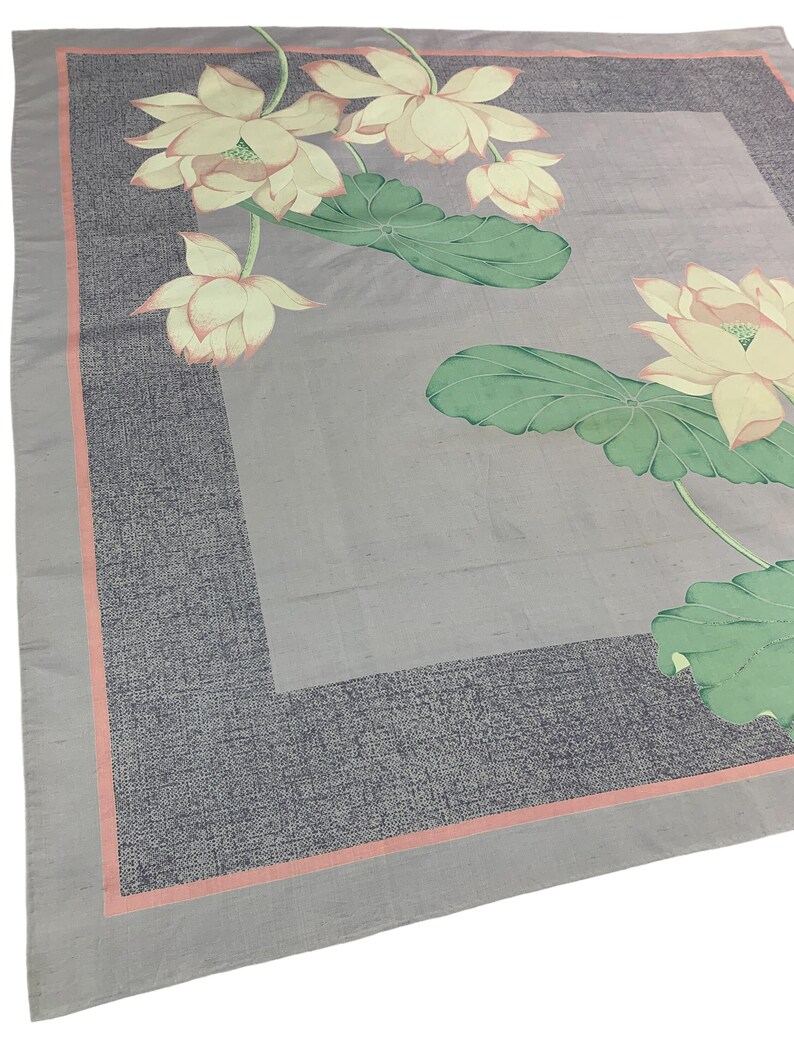 May include: A square, light gray scarf with a floral design. The scarf features a border of dark gray with a thin, salmon-colored stripe. The floral design includes lotus flowers in shades of cream and pink, with green leaves.