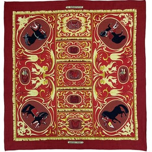 Puede incluir: Un pañuelo de seda rojo con un patrón repetido de caballos, jinetes y elementos decorativos en amarillo y crema. El pañuelo presenta el texto "LA PRESENTATION" y "HERMES, PARIS".