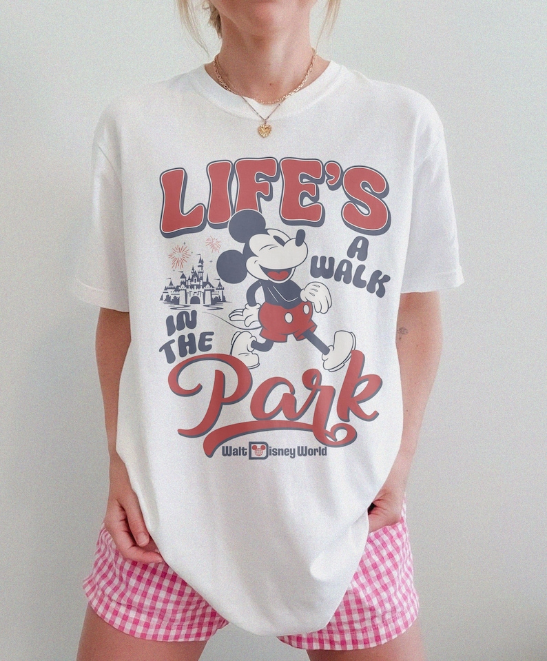 May include: White t-shirt featuring a retro design with Mickey Mouse and the text "LIFE'S A WALK IN THE PARK" in red and blue. The Walt Disney World logo is at the bottom. The shirt is a classic, casual style.