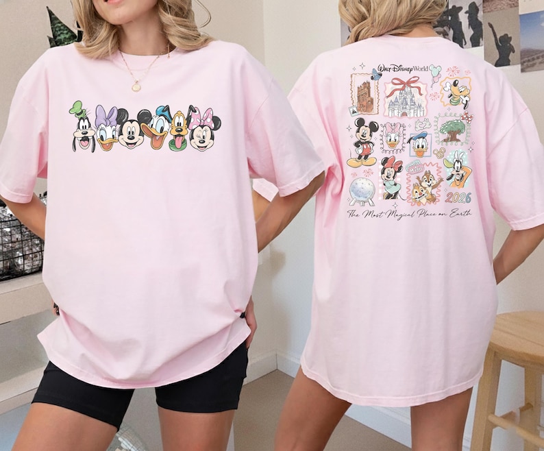 May include: A light pink t-shirt featuring Disney characters' faces across the front. The back of the shirt displays a collage of Disney World-themed images and text, including "Walt Disney World" and "The Most Magical Place on Earth."