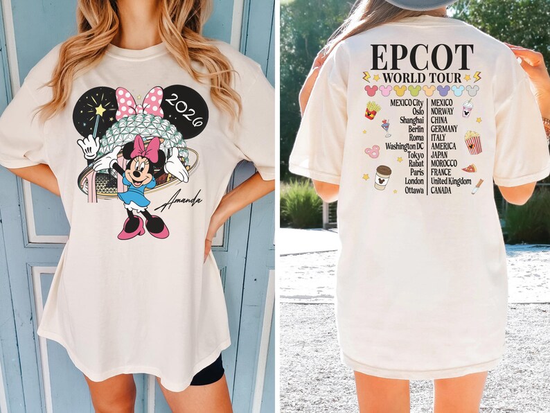 May include: Cream-colored t-shirt featuring a Minnie Mouse graphic with a pink bow, blue dress, and a wand. The text "2026" is above the character. The back of the shirt displays "EPCOT WORLD TOUR" and various city names.