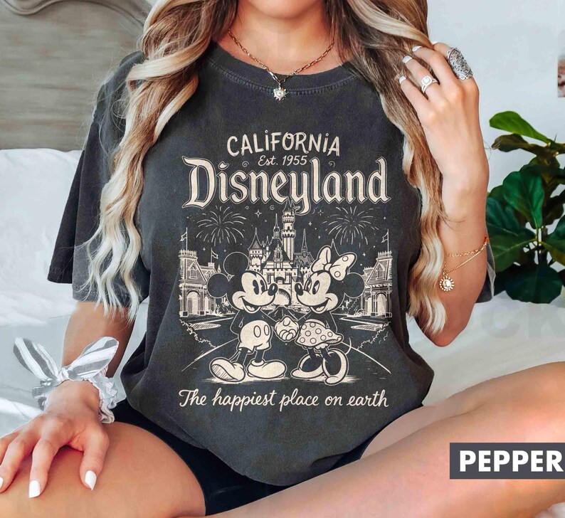 May include: Dark grey t-shirt with a Disneyland graphic. The design features Mickey and Minnie Mouse, a castle, fireworks, and the text "California Disneyland Est. 1955" and "The happiest place on earth."