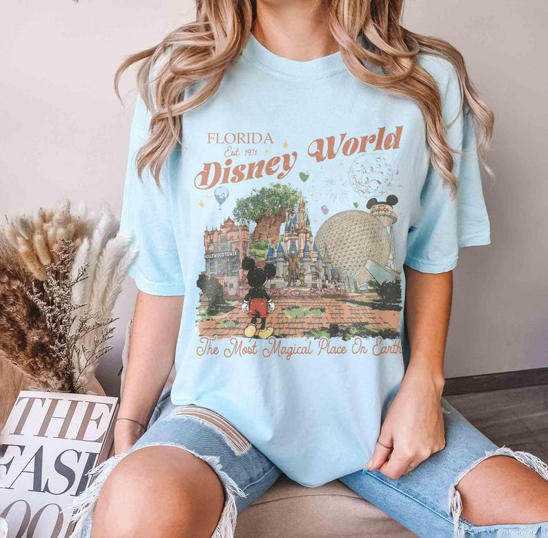 May include: Light blue t-shirt featuring a Disney World graphic. The design includes Mickey Mouse, a castle, and the text "Florida Disney World" and "The Most Magical Place On Earth".