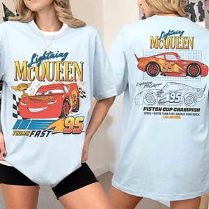 May include: Light blue t-shirt featuring Lightning McQueen from the Cars movie. The front graphic shows McQueen with the number 95 and the text "Think Fast". The back displays McQueen and the text "Piston Cup Champion".