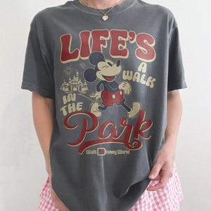 May include: Gray t-shirt featuring Mickey Mouse with the text "Life's a Walk in the Park" in red and cream lettering. The design includes an image of Cinderella's castle and the Walt Disney World logo.