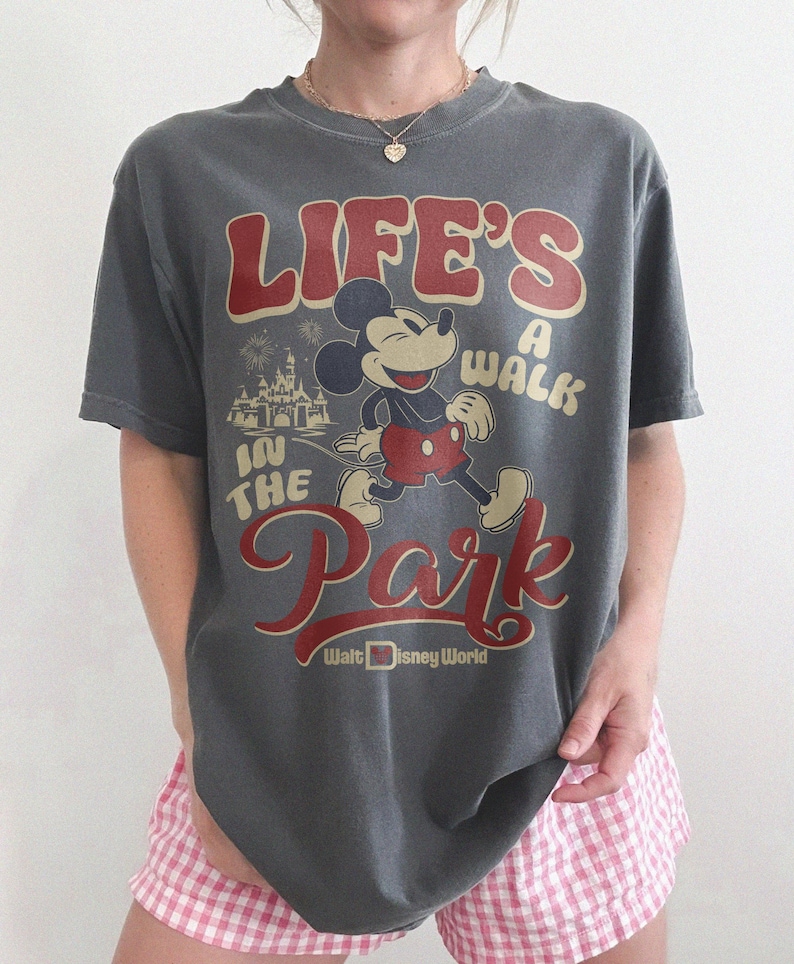 May include: Gray t-shirt featuring Mickey Mouse with the text "Life's a Walk in the Park" in red and cream lettering. The design includes an image of Cinderella's castle and the Walt Disney World logo.