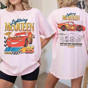 May include: Pink t-shirt featuring Lightning McQueen from the Cars movie. The front graphic shows McQueen with the text "Lightning McQueen" and "95". The back of the shirt has a graphic of McQueen and the text "Piston Cup Champion".