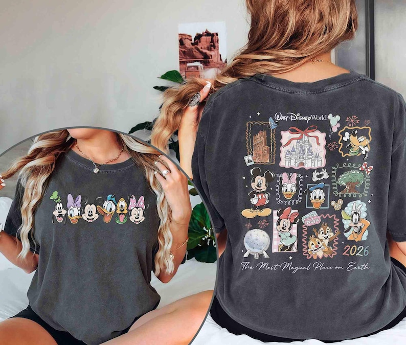 May include: Dark gray t-shirt featuring Disney characters on the front and back. The front displays a row of cartoon faces. The back has a collage of Disney World images and characters, with the text "Walt Disney World" and "2026".