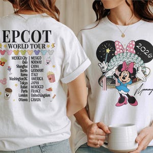 May include: White t-shirts with colorful graphics. One features Minnie Mouse with a bow and the text "2026" and "Mommy." The other shirt has "EPCOT WORLD TOUR" and a list of cities. The shirts are casual wear.