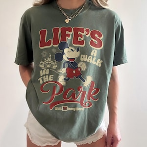 May include: Green t-shirt featuring Mickey Mouse and the text "LIFE'S A WALK IN THE PARK" with "Walt Disney World" below. The graphic includes a cartoon of Mickey Mouse and a castle. The shirt is a solid green color.