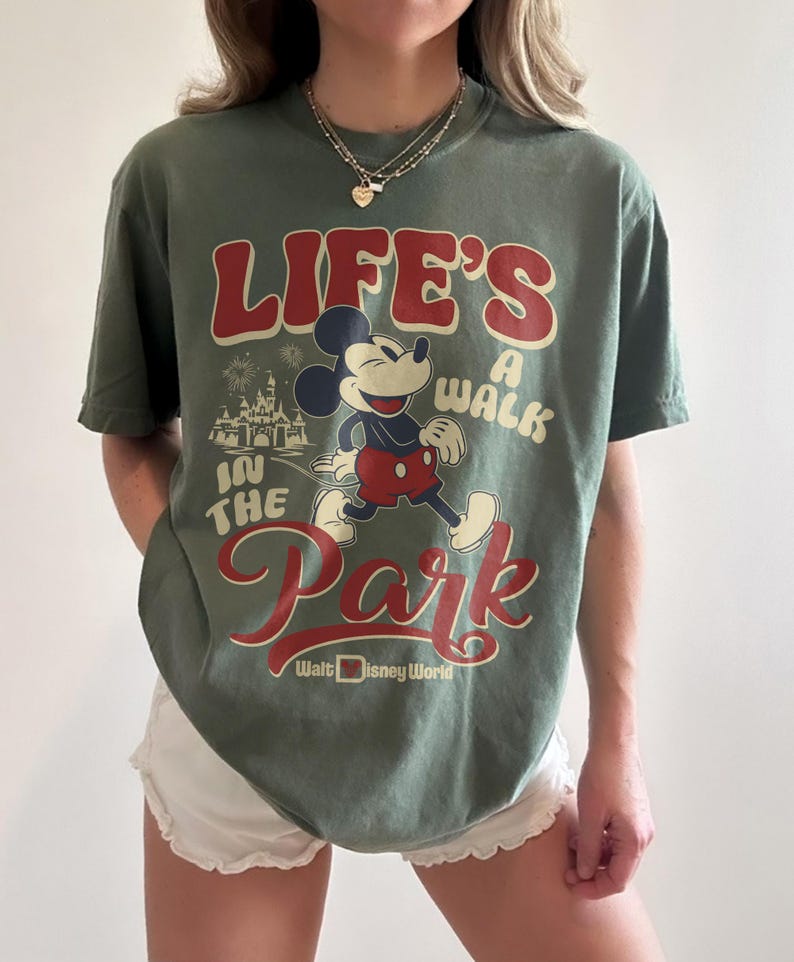 May include: Green t-shirt featuring Mickey Mouse and the text "LIFE'S A WALK IN THE PARK" with "Walt Disney World" below. The graphic includes a cartoon of Mickey Mouse and a castle. The shirt is a solid green color.