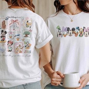 May include: White t-shirts featuring Disney characters. One shirt has a collage of characters and landmarks with "Walt Disney World" and "The Most Magical Place on Earth" text. The other shirt has character faces.
